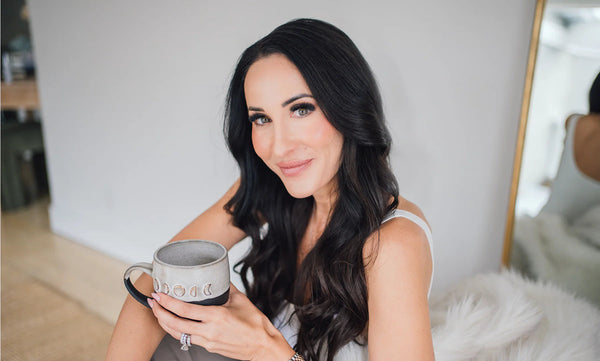 Dark-haired woman holding a ceramic mug in a softly lit room.