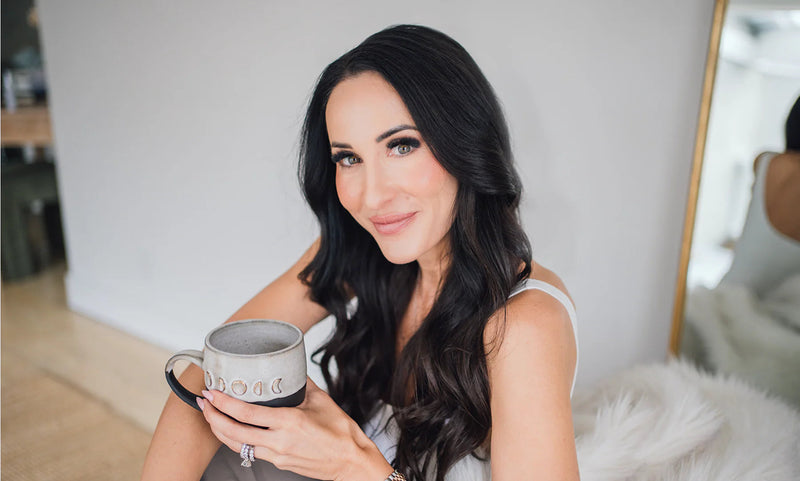 Dark-haired woman holding a ceramic mug in a softly lit room.